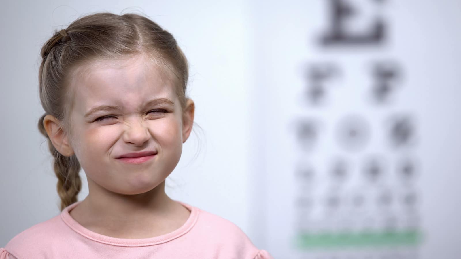 Young girl squinting with an eye chart in the background