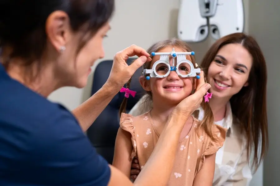 Young girl having her vision checked with trial glasses, with her parent beside her