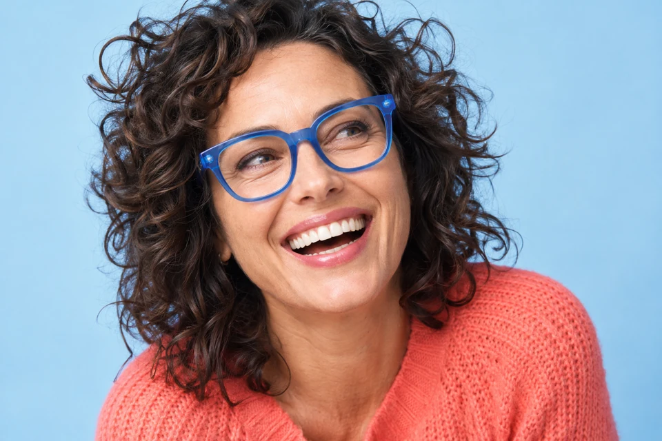 Laughing woman wearing bold blue glasses against a sky-blue backdrop